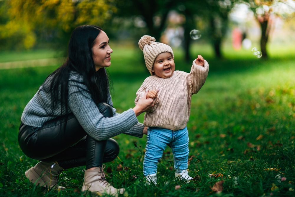 A parent and smiling toddler playing with bubbles in a park